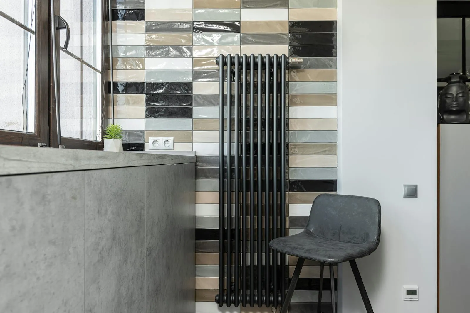A black column radiator on a tiled wall — larger radiators let the heat pump run cooler, and cooler means cheaper to run.
